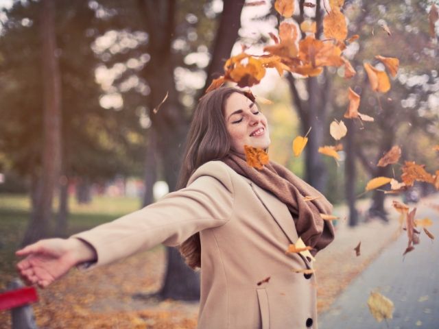 щастлива жена хвърля есенни листа - снимка