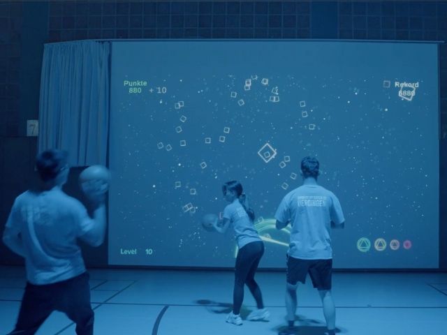 трима възрастни играят на интерактивна игра пред голям екран - снимка 