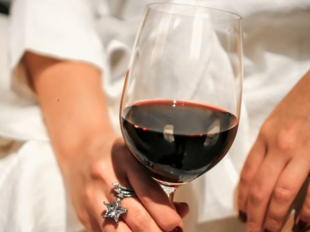 Женска ръка държи ччаша с червено вино