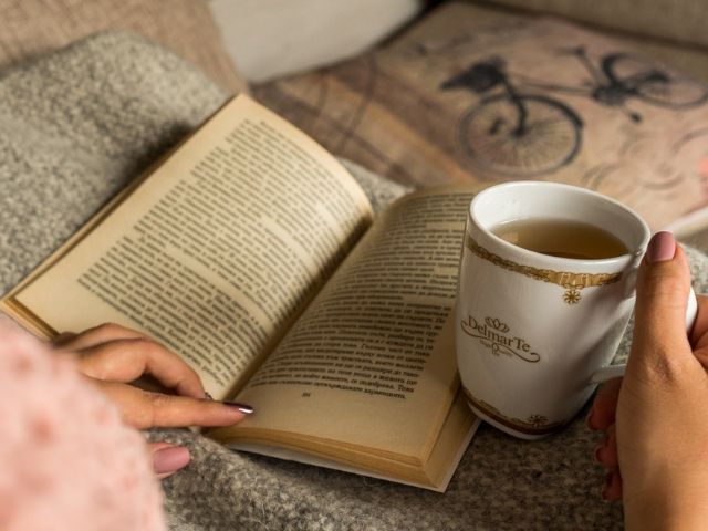 жена държи чаша чай с книга в ръка - снимка