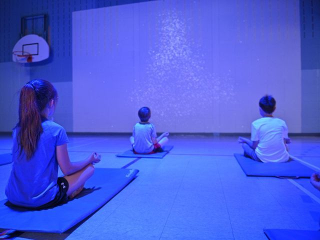 деца практикуват йога пред интерактивен екран в зала - снимка