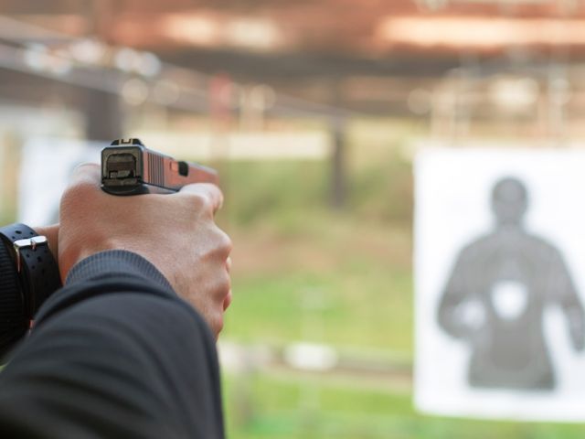 мъжки ръце държат пистолет насочен към мишена - снимка